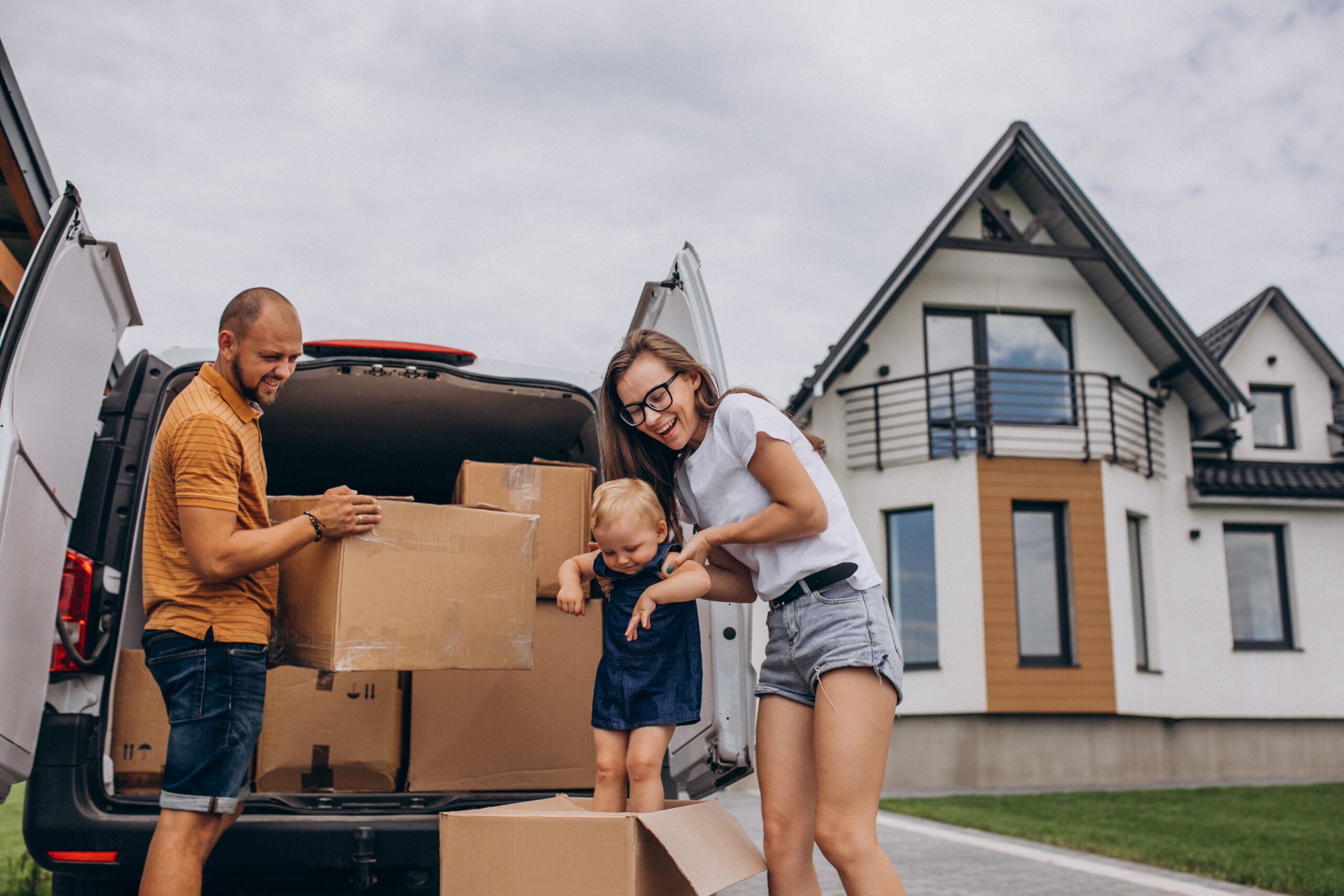 A young family unloading boxes from their car in front of their new home, representing Insurance and Surety Bonds Beaumont TX for protecting what matters most.